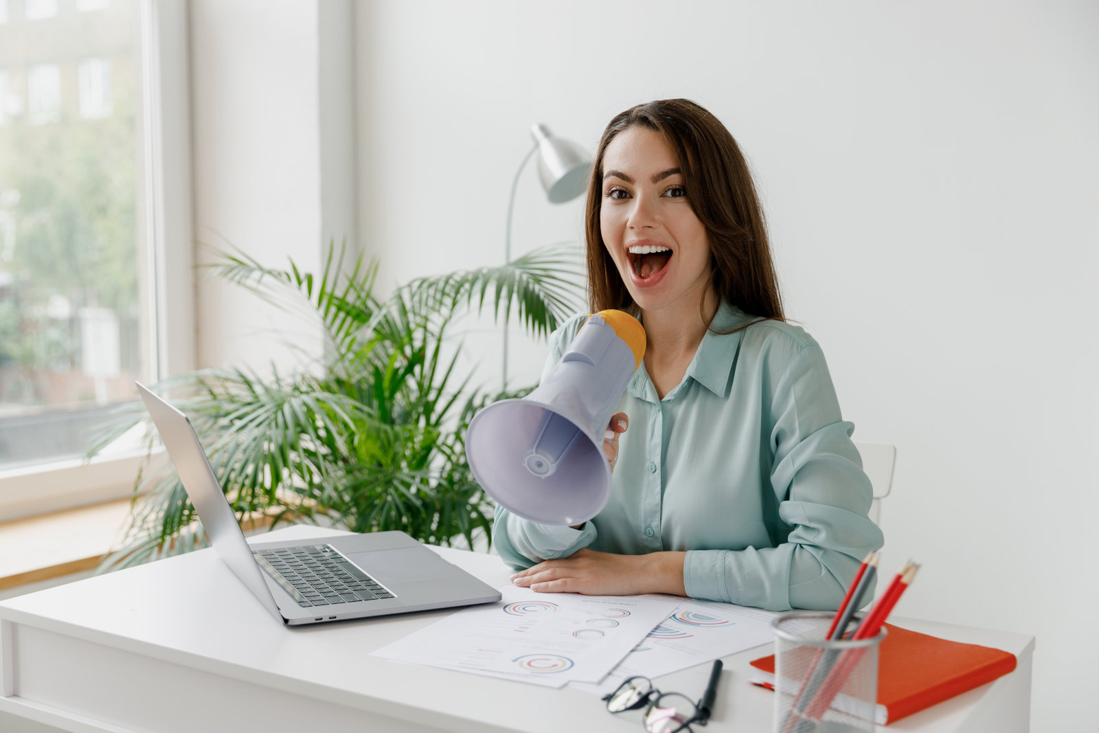 Photo of a business woman making an announcement in front of a computer with a megaphone