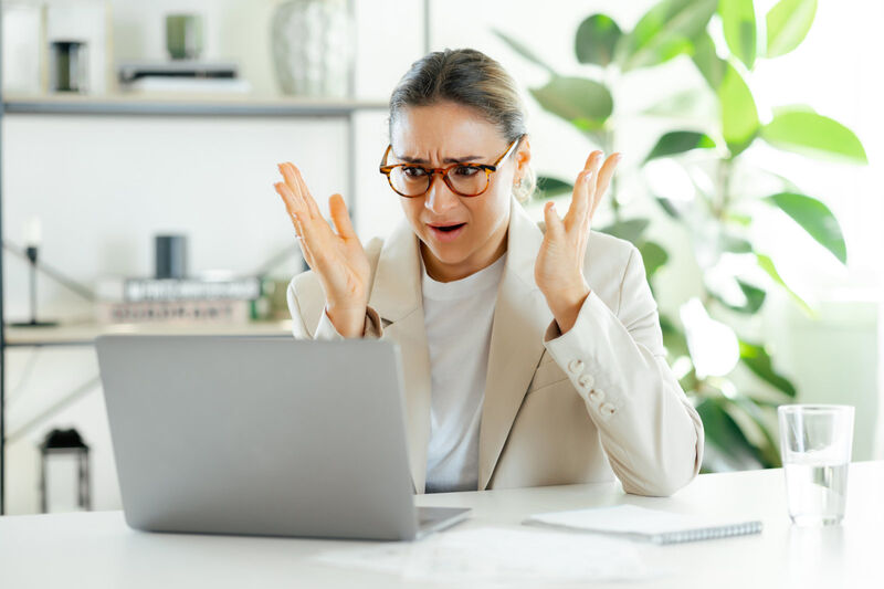 Confused frustrated businesswoman throws her hands up in the air, upset while looking at her laptop as a result of bad work