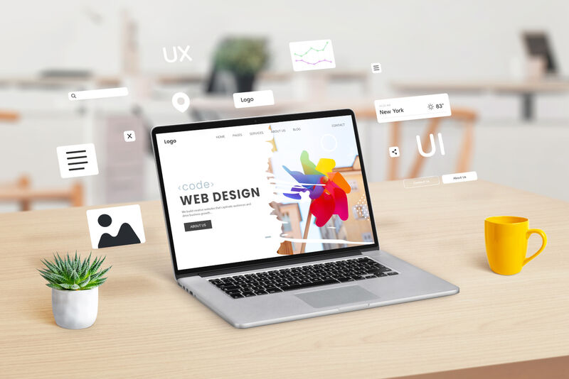 Laptop on a workspace displaying a web design studio webpage, with graphic web modules and elements floating around, illustrating the concept of dynamic website creation and design integration