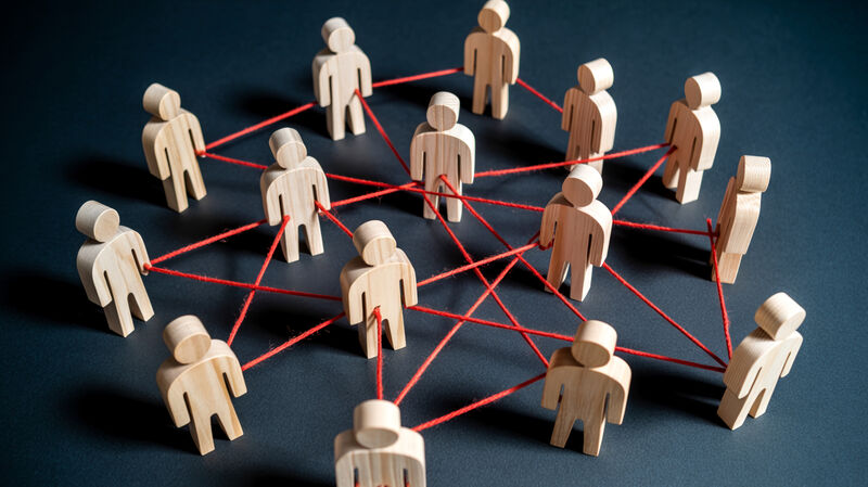 Wooden human figures connected by red threads form a complex network on a dark surface with dramatic lighting symbolizing teamwork collaboration and communication