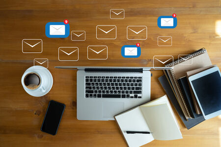 A picture showing a laptop with lots of emails around it and other items such as coffee, phone and notebook that are used when being creative